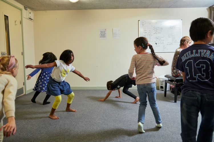 Six young children are making shapes with their arms and legs. One of them is crawling on the ground.